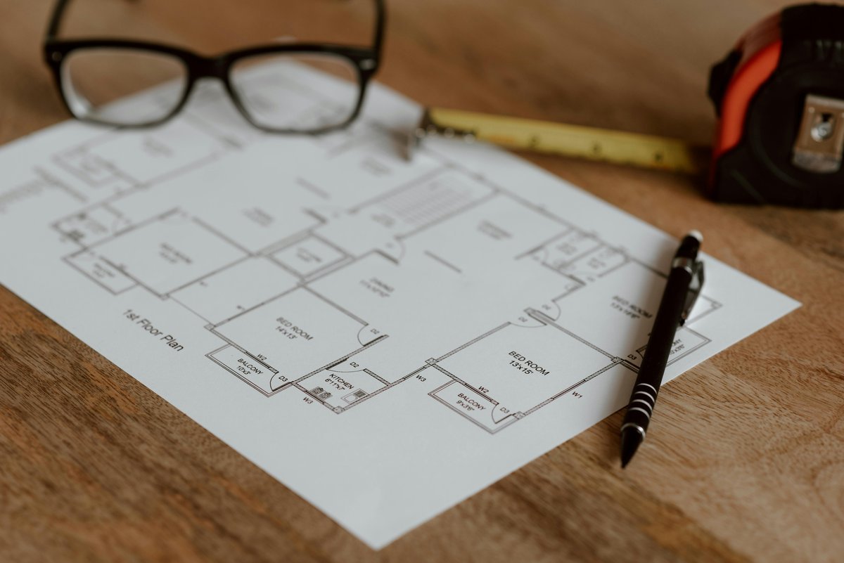 Apartment floor plan on a wooden table with glasses, a tape measure and a pen beside it
