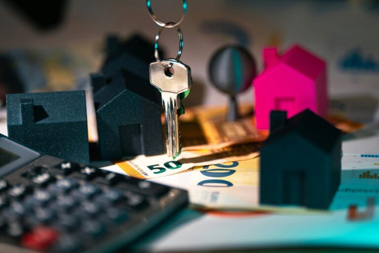 Key hanging over a calculator, euro banknotes and miniature houses, one of them pink