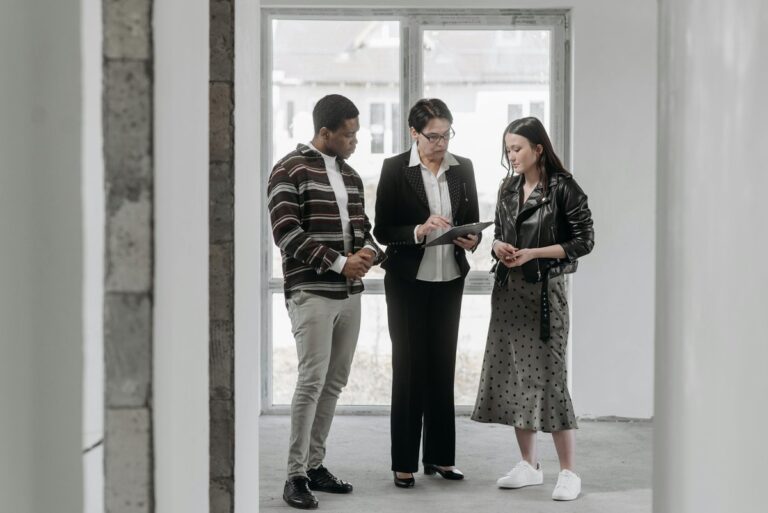 Troje ludzi stoi w pustym wnętrzu przy oknie i patrzy na tablet trzymany przez kobietę w okularach